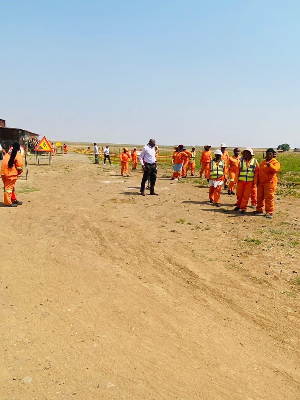 Group of construction workers in orange uniforms standing on a dirt road during daytime.