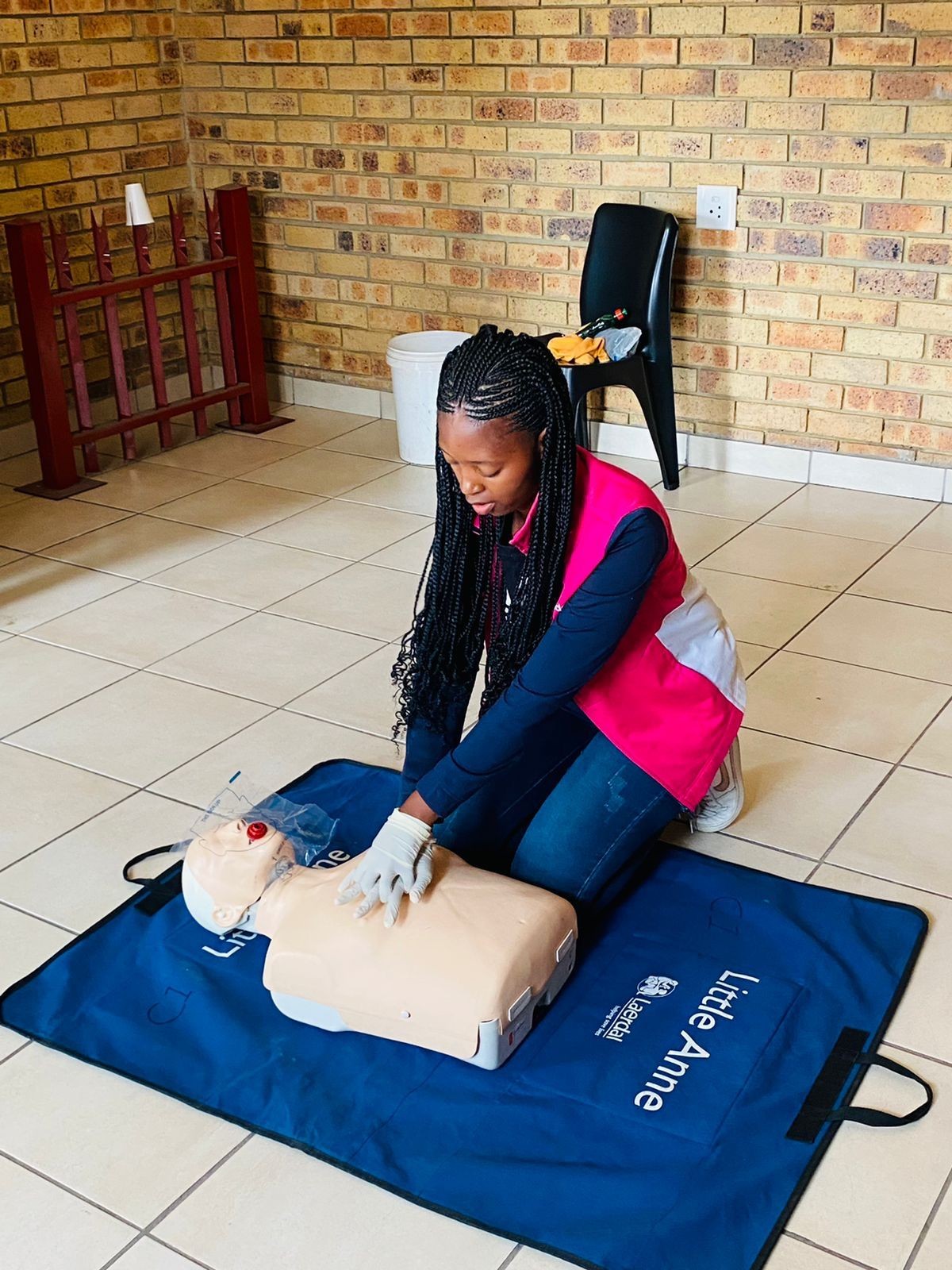 Person practicing CPR on a dummy mannequin lying on a blue mat in a room with brick walls.