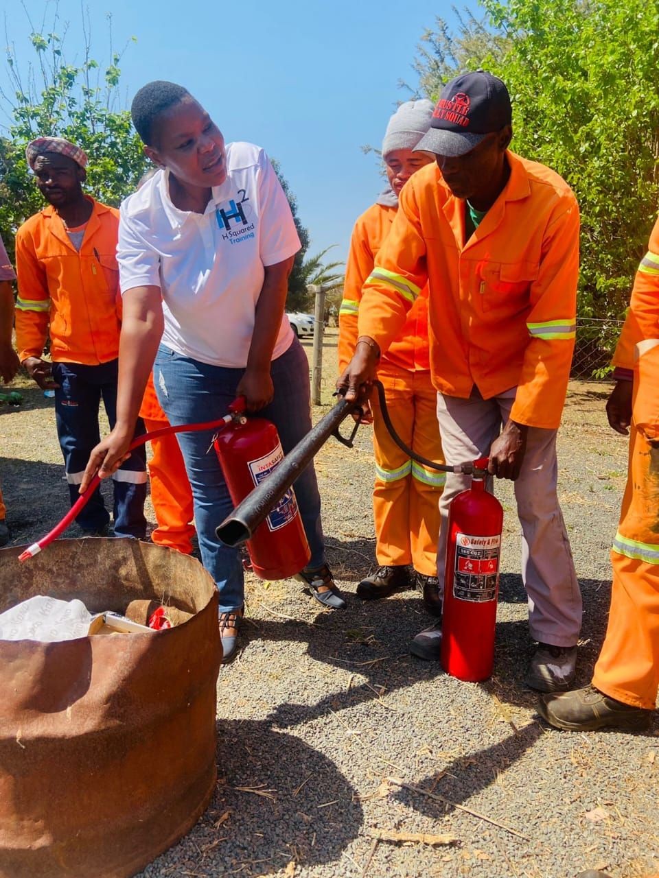 Training session with people in orange uniforms learning to use fire extinguishers outside.